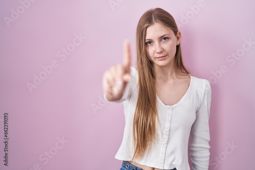 Young caucasian woman standing over pink background pointing with finger up and angry expression  showing no gesture