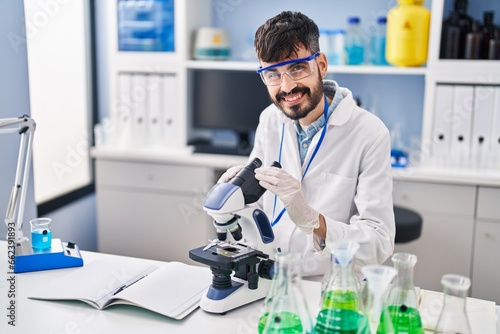 Young hispanic man scientist using microscope working at laboratory