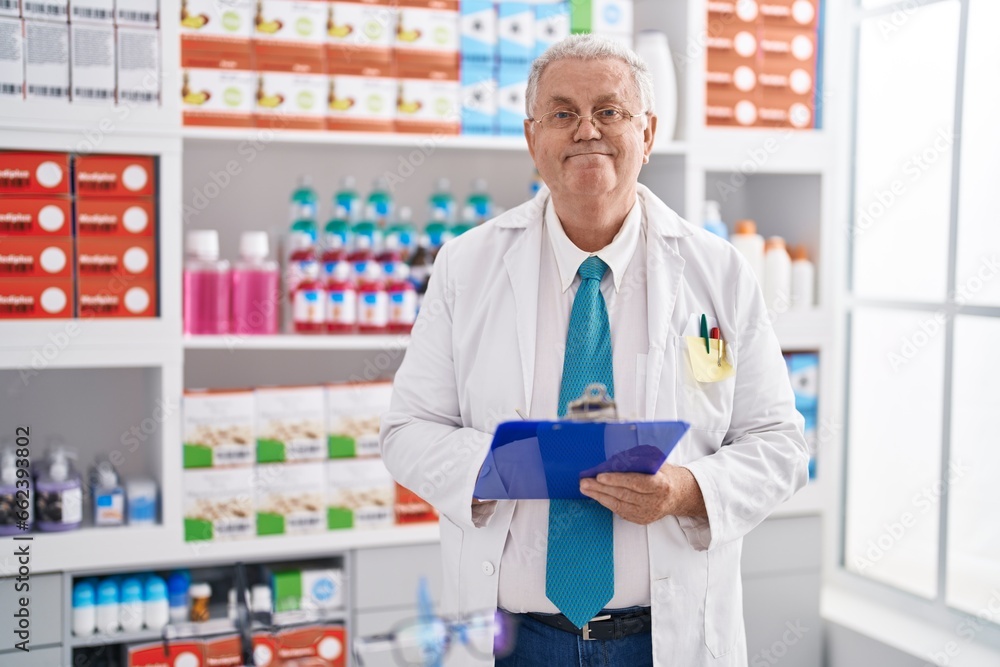 Middle age grey-haired man pharmacist writing on document at pharmacy Middle age grey-haired man pharmacist writing on document at pharmacy