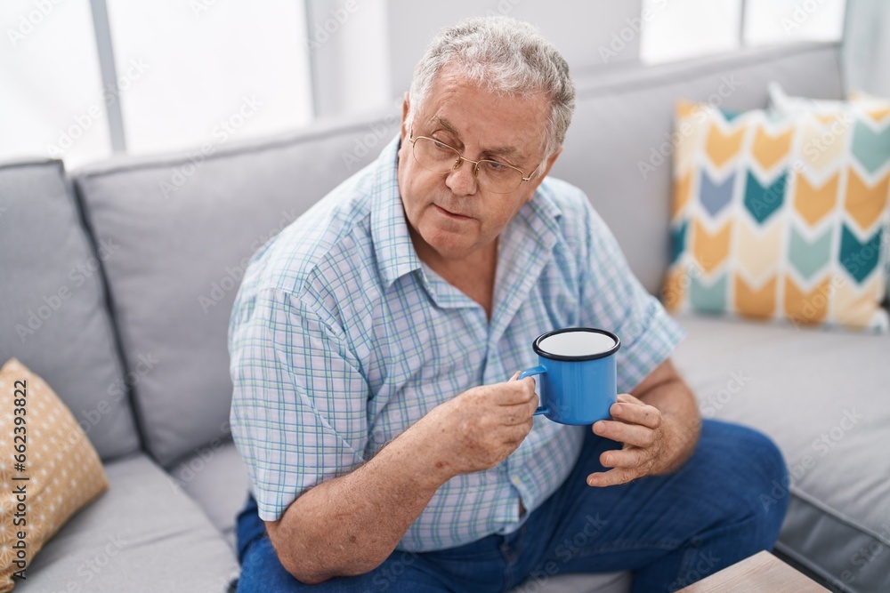 Middle age grey-haired man drinking coffee sitting on sofa at home Middle age grey-haired man drinking coffee sitting on sofa at home