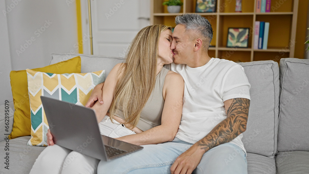 Man and woman couple using laptop sitting on sofa kissing at home Man and woman couple using laptop sitting on sofa kissing at home