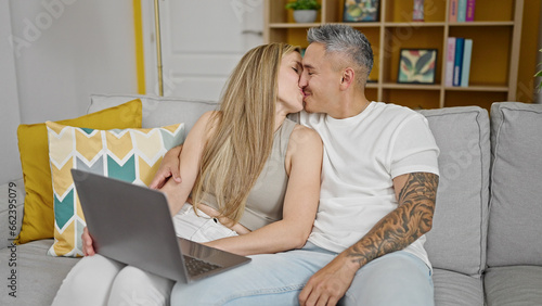 Man and woman couple using laptop sitting on sofa kissing at home