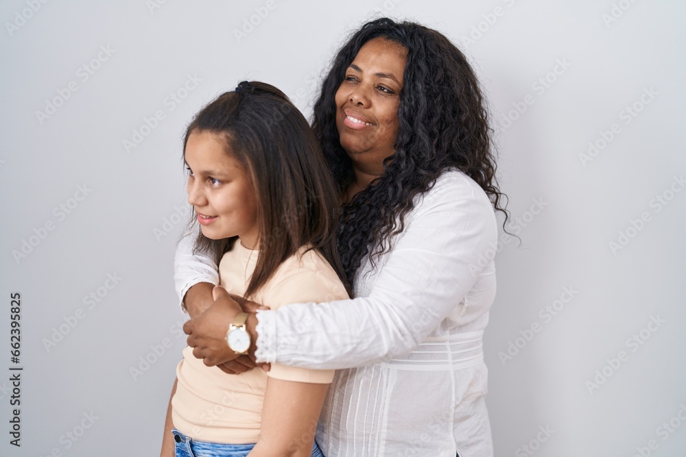 Mother and young daughter standing over white background looking to side, relax profile pose with natural face and confident smile. Mother and young daughter standing over white background looking to side, relax profile pose with natural face and confident smile.