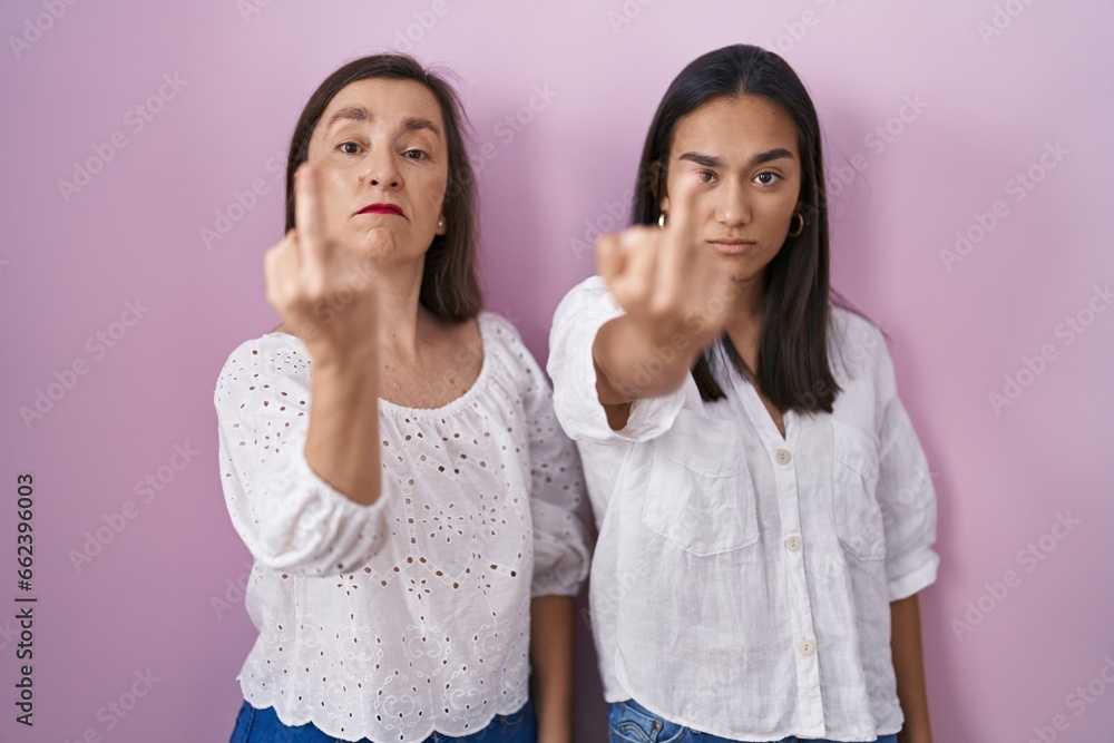 Hispanic mother and daughter together showing middle finger, impolite and rude fuck off expression Hispanic mother and daughter together showing middle finger, impolite and rude fuck off expression
