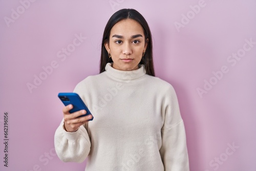Fotografie Young south asian woman using smartphone thinking attitude and sober expression