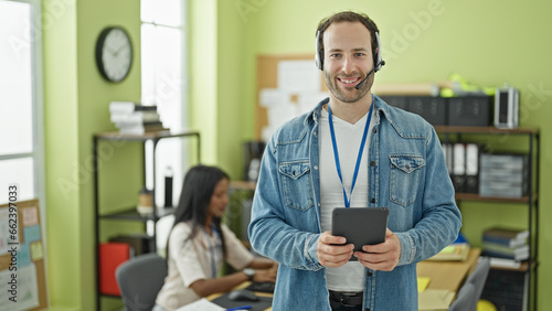 Two workers man and woman using touchpad and headphones working at the office