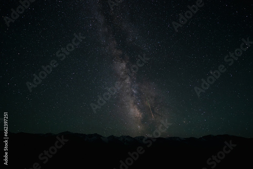 The Milky Way with a falling meteorite on the background of mountains. A bright colored stripe is a trace of a meteorite. Lots of stars. The peaks are covered with snow. Space. Photo for screensaver