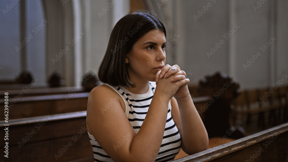 Young beautiful hispanic woman praying on a church bench at Augustinian Church in Vienna Young beautiful hispanic woman praying on a church bench at Augustinian Church in Vienna