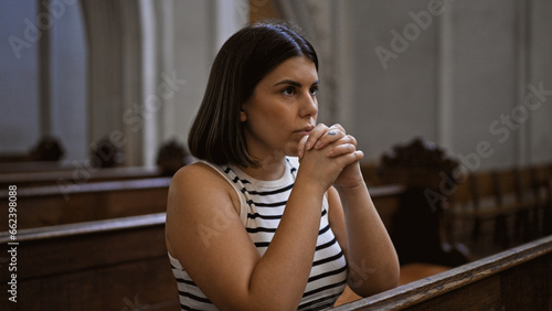 Young beautiful hispanic woman praying on a church bench at Augustinian Church in Vienna