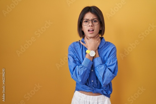 Young girl standing over yellow background shouting suffocate because painful strangle. health problem. asphyxiate and suicide concept.