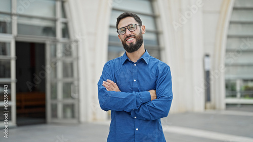 Young hispanic man business worker standing with arms crossed gesture at street