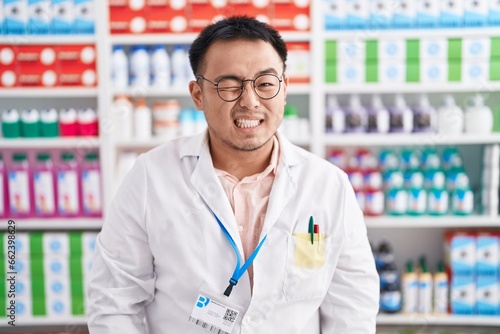 Chinese young man working at pharmacy drugstore winking looking at the camera with sexy expression, cheerful and happy face. © Krakenimages.com