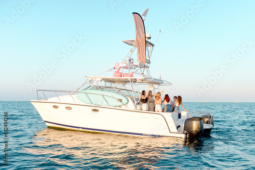 A group of young people drinking champagne and alcohol, having fun, dancing on the platform of a catamaran yacht in the sea in the sunlight