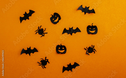 Halloween background, paper black bats, pumpkins and spiders on orange background.