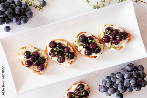 Crostini appetizers with roasted grapes and whipped feta cheese. Overhead view table scene against a white marble background. Party food concept. photo