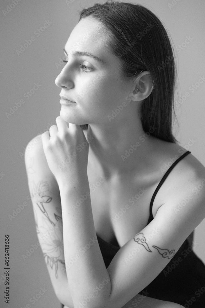 Black and white portrait of a brunette girl without make up on a grey backgroung in a black summer clothes. Woman is sitting on a chair Black and white portrait of a brunette girl without make up on a grey backgroung in a black summer clothes. Woman is sitting on a chair