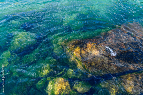 Steine und Felsen unter Wasser mit Algen oder Moos bedeckt. Natürlich reflektiertes Sonnenlicht. © Elena