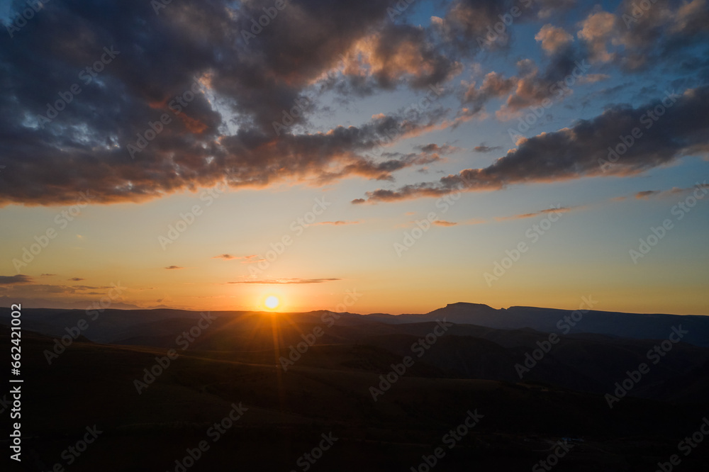 A beautiful golden sunset in the mountains. The sun is sinking behind the mountains, coloring the horizon with rays. Shooting from a drone. A beautiful golden sunset in the mountains. The sun is sinking behind the mountains, coloring the horizon with rays. Shooting from a drone.