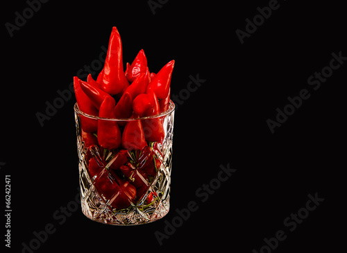 A glass full of red hot peppers on a dark background.