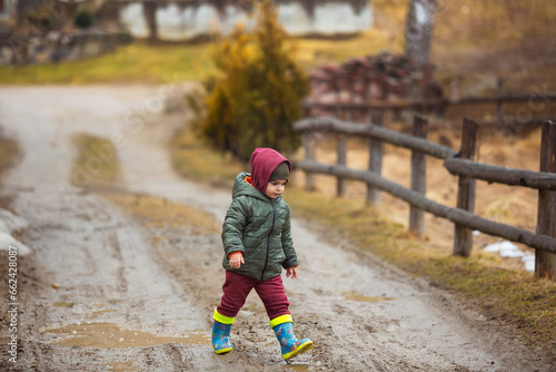 Little boy in protective rubber boots and rain clothes jumping in mud puddle. Happy child having fun while playing in puddle after rain.