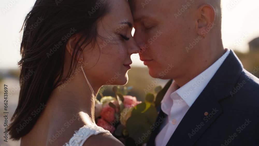 Lovely bride and groom rubbing noses at romantic photoshoot after wedding ceremony. Happy couple in love tenderly embracing on honeymoon. Attractive man, woman posing at the sea shore. Close-up. Lovely bride and groom rubbing noses at romantic photoshoot after wedding ceremony. Happy couple in love tenderly embracing on honeymoon. Attractive man, woman posing at the sea shore. Close-up.