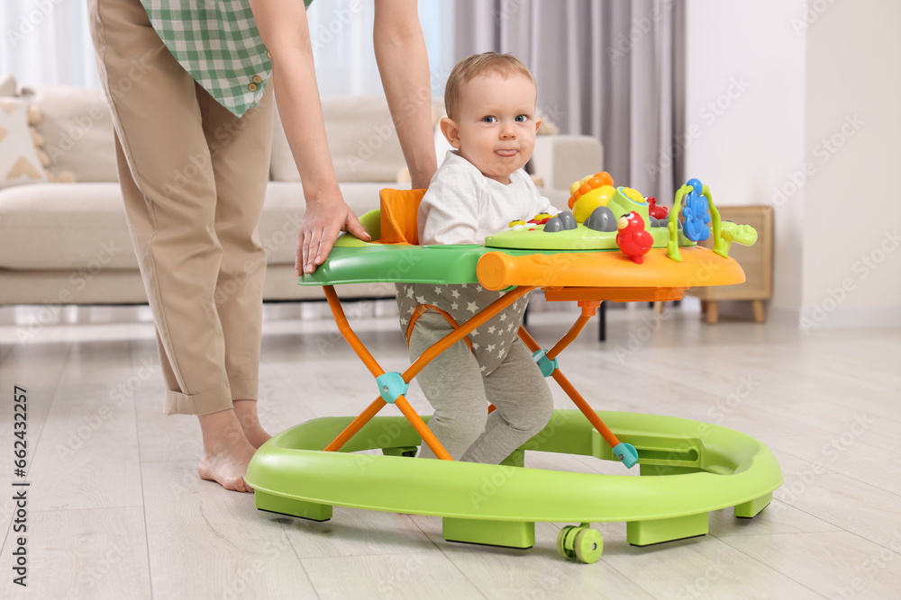 Cute boy making first steps with baby walker. Mother and her little son spending time together at home Cute boy making first steps with baby walker. Mother and her little son spending time together at home
