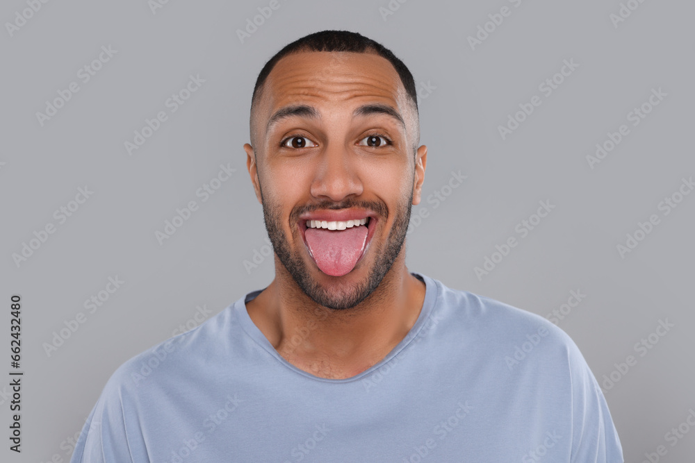 Happy young man showing his tongue on light grey background Happy young man showing his tongue on light grey background
