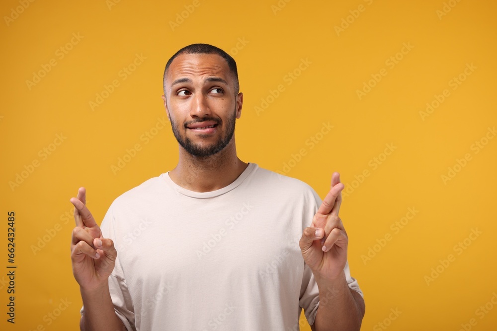 Young man crossing his fingers on orange background, space for text Young man crossing his fingers on orange background, space for text