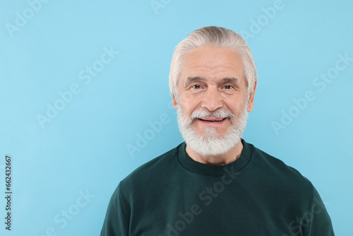 Portrait of handsome senior man on light blue background. Space for text