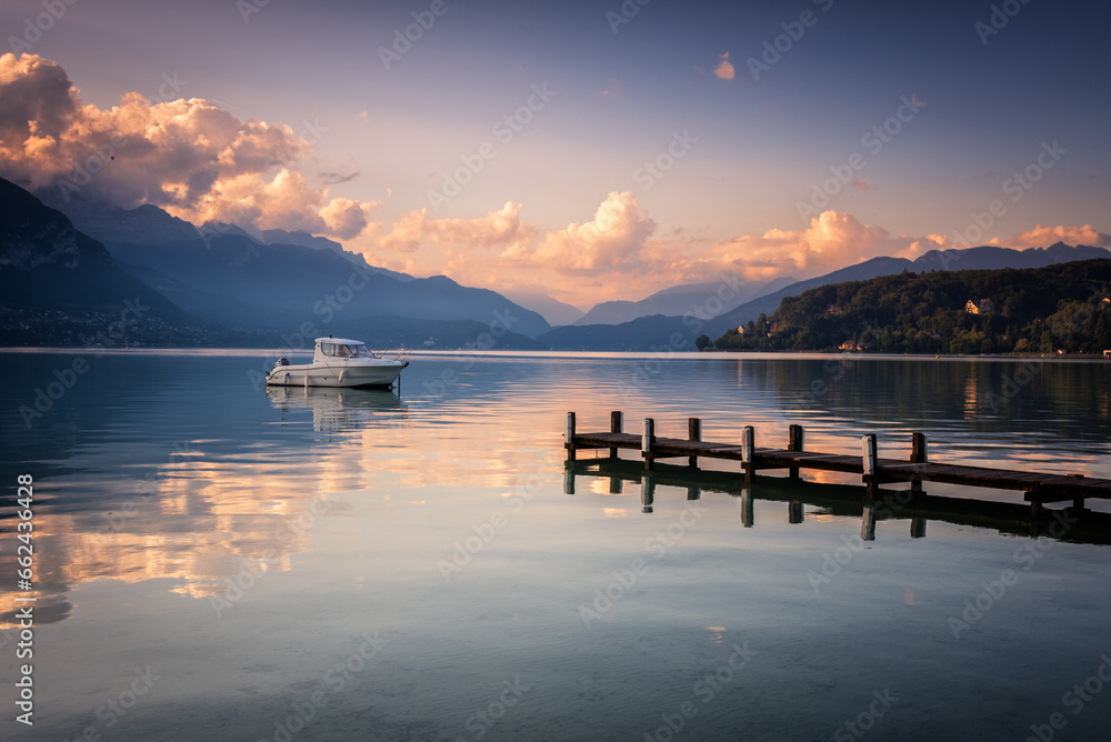Boat next to a dock in the calm waters of Lake Annecy and the Alps mountain range in the background at sunset, Lake Annecy, Auvergne - Rhône - Alps, France, Europe