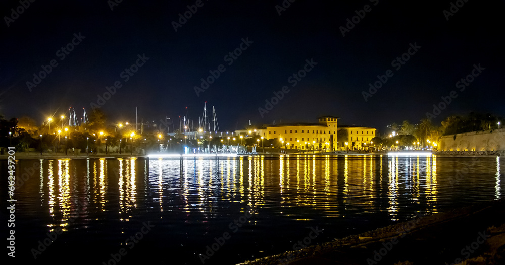 night city, city lights, and Mallorca fortress reflected in the water of the artificial lake at night against the dark sky.