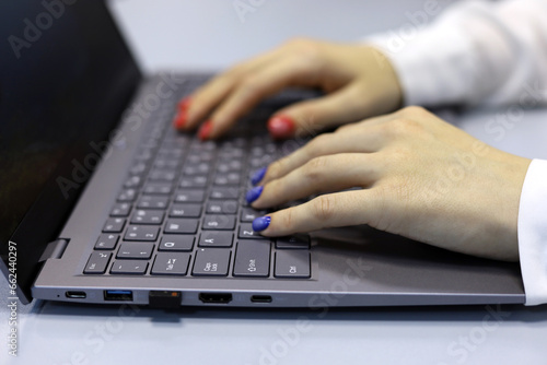 Female hands on laptop at desk. Woman types on notebook keyboard, nails with manicure of red and blue colors