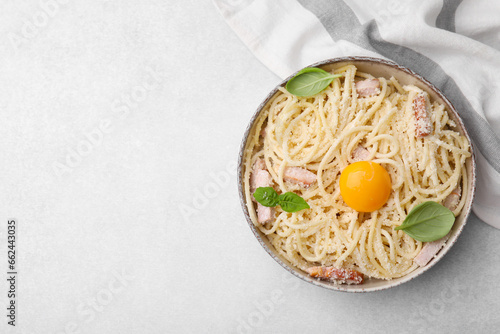 Bowl of tasty pasta Carbonara with basil leaves and egg yolk on light grey table, top view. Space for text