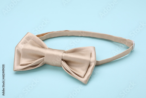Stylish beige bow tie on light blue background, closeup