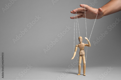 Man pulling strings of puppet on gray background, closeup. Space for text