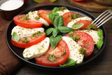 Plate of delicious Caprese salad with pesto sauce on wooden table, closeup