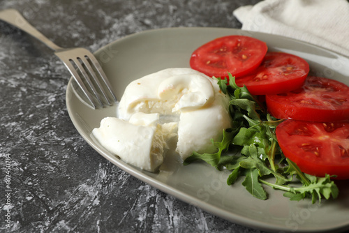 Delicious burrata cheese with tomatoes, arugula and fork on grey table, closeup