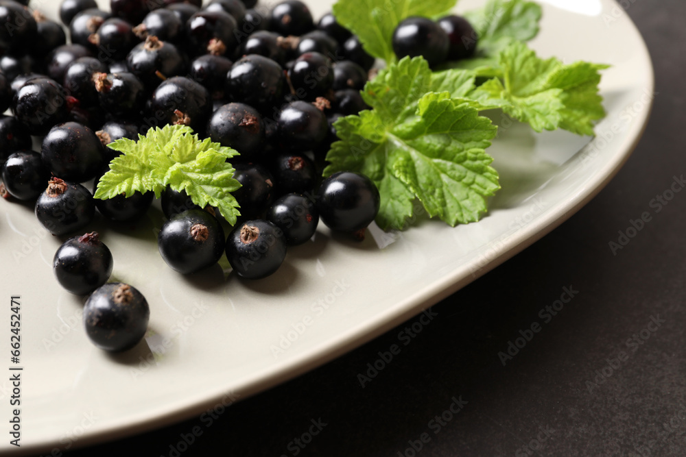Plate with ripe blackcurrants and leaves on dark background, closeup Plate with ripe blackcurrants and leaves on dark background, closeup
