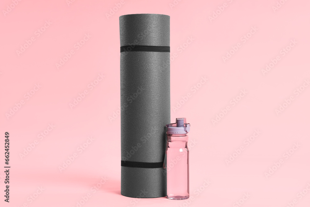 Grey yoga mat and bottle of water on pink background Grey yoga mat and bottle of water on pink background