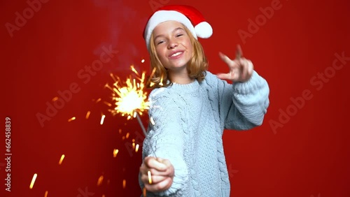 funny girl in Santa Claus cap holding sparkler on the red background. Concept Christmas