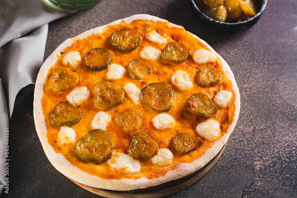 Spicy pizza with cheese and pickles on a wooden board on the table Spicy pizza with cheese and pickles on a wooden board on the table