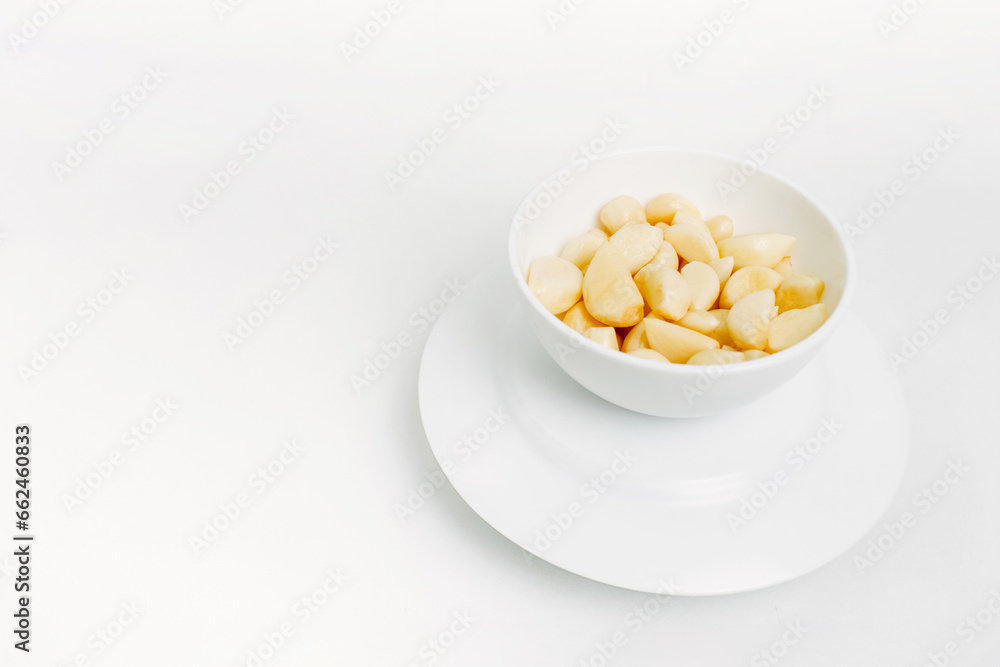 Peeled garlic cloves in a white plate on a white background. Peeled garlic cloves in a white plate on a white background.