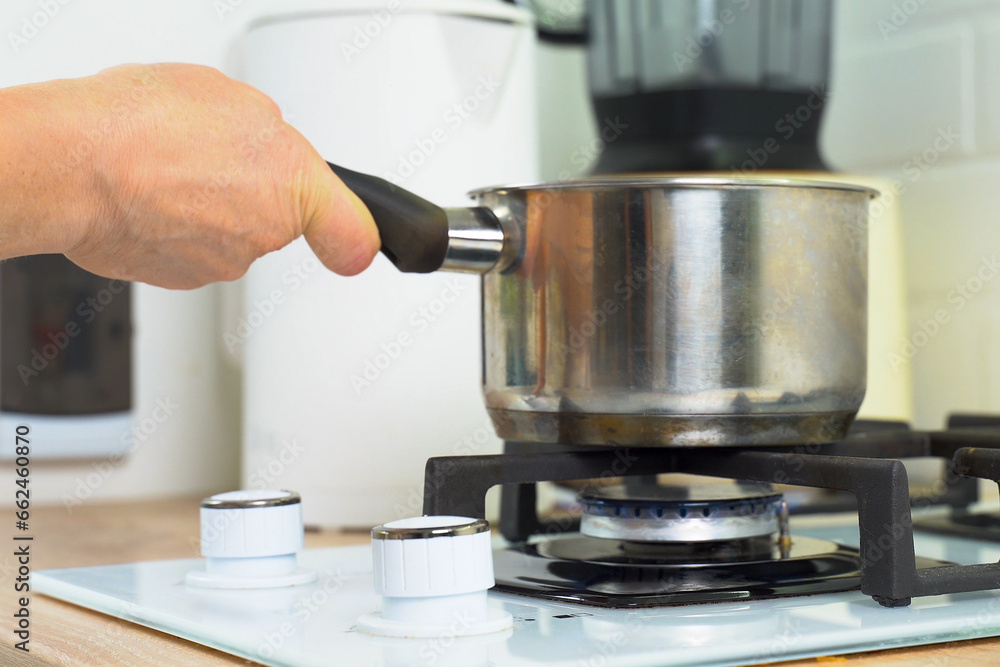 A woman places a cooking pot on a burning gas stove. A woman places a cooking pot on a burning gas stove.