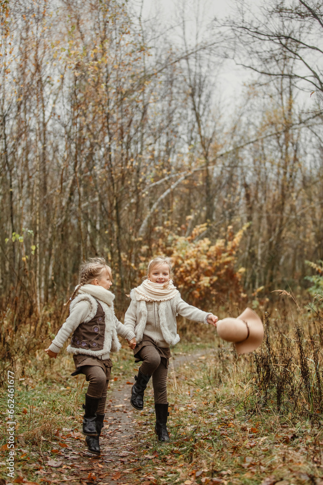 Fototapeta premium Twin girls play in the autumn park, throw their hats up.