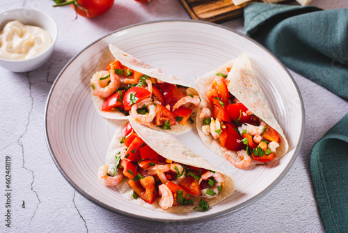 Soft appetizer mini tacos with shrimp, tomatoes and herbs on a plate