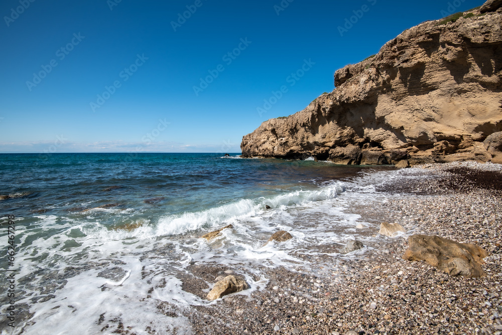 Empty pebble tropical beach under white cliffs against blue sky. Copy space