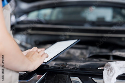 Licensed technician in garage using tablet to follow checklist while doing maintenance on car. Close up shot of expert in auto repair shop doing checkup on vehicle radiator © DC Studio