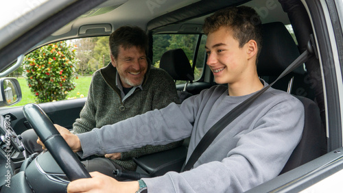 Father teaching his teenage son to drive, both joyfully bonding.