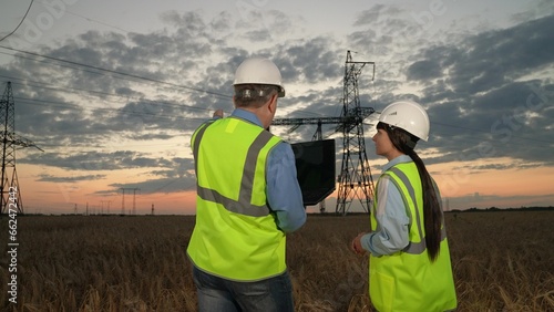 Engineer points by hand on power transmission lines to young trainee in evening