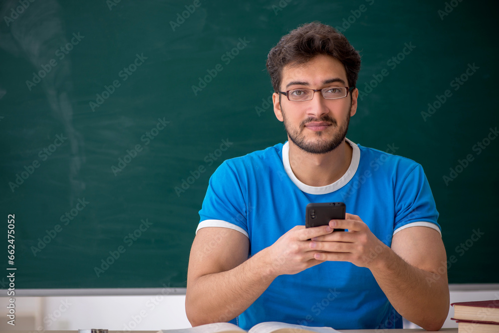 Young male student holding smartphone in the classroom Young male student holding smartphone in the classroom